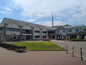 阿寒マルシェと宿泊施設「赤いベレー」の外観。白い建物の前にはベンチがあり、広々とした芝生が広がっている。