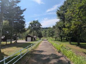 道の駅阿寒丹頂の里の裏手にある散策路。舗装された小道が森の中へ続いており、周囲には木々が茂っている。