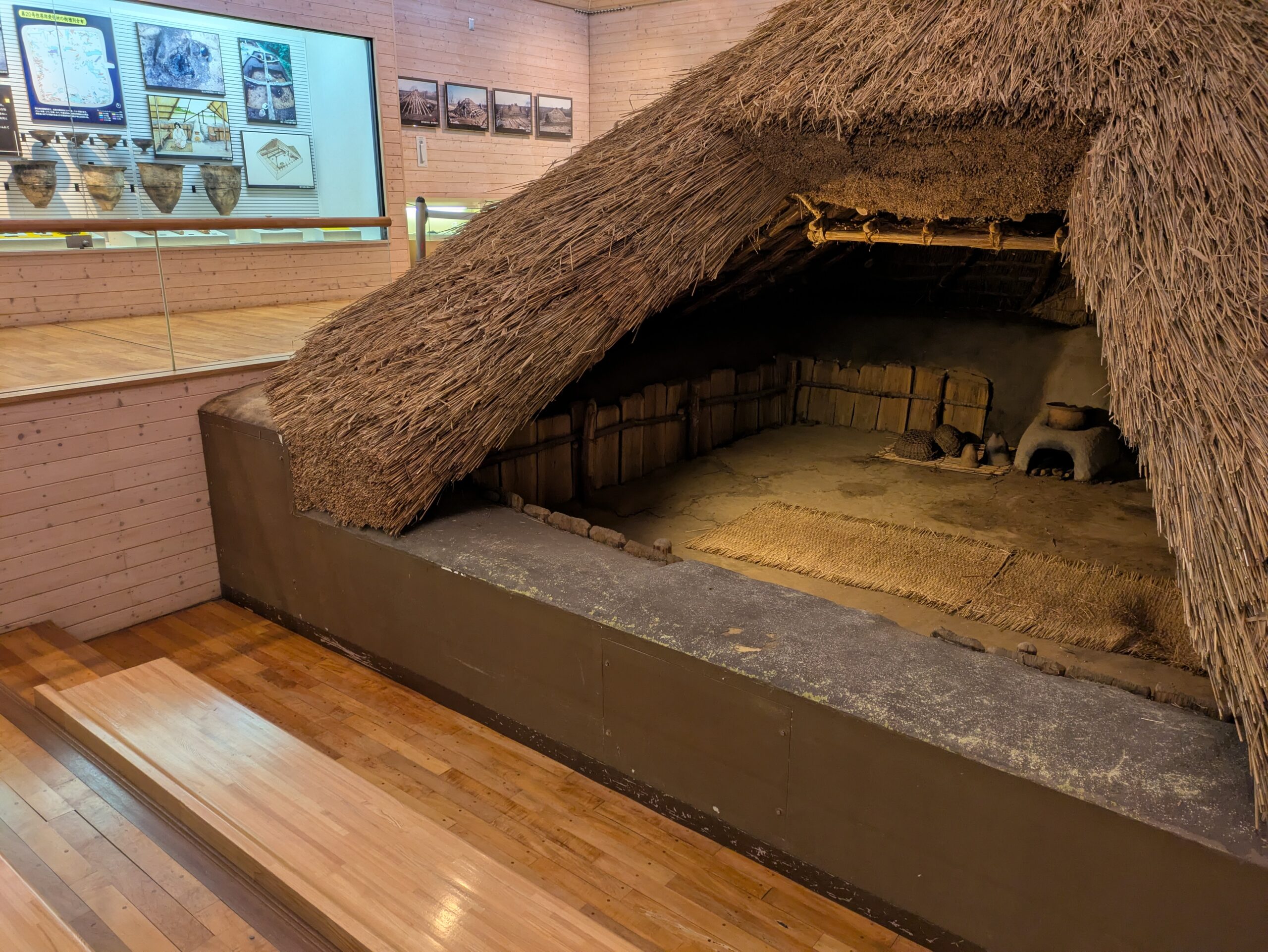 住居の中へ|火のそばに生きる暮らし 竪穴住居の内部。茅葺きの屋根の下に、土の床や生活道具が再現されています。